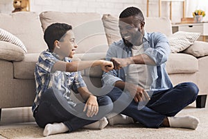 Cheerful Black Preteen Boy Fist Bumping With His Dad At Home