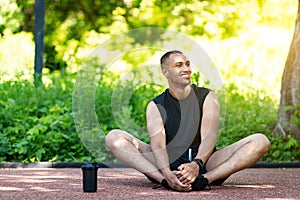 Cheerful black sportsman stretching after running at green park, empty space