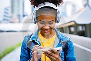Cheerful black student girl wearing headset and using mobile smartphone