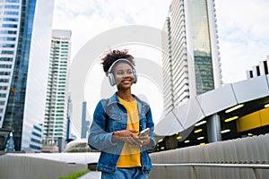 Cheerful black student girl wearing headset and using mobile smartphone