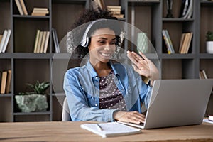 Cheerful Black student girl in wireless headphones waving hand hello