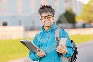 Cheerful black student guy using smartphone smiling to camera outdoor