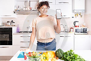 Cheerful black woman holding smartphone with white copy space screen in the kitchen