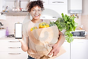Cheerful black woman holding smartphone with white copy space screen in the kitchen