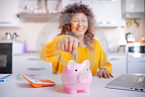Cheerful black woman saving money for the future, focus on piggy bank