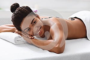 Cheerful black woman in spa salon with hot stones