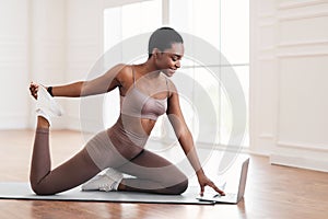 Cheerful black woman stretching leg muscles using laptop