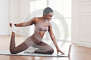 Cheerful black woman stretching leg muscles using laptop computer