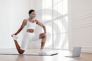 Cheerful black woman stretching leg muscles using pc