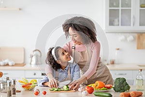 Cheerful black woman teaching girl how to prepare salad