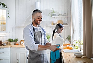 Cheerful black woman washing dishes while her husband wiping them at kitchen, copy space