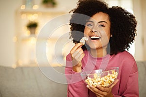 Cheerful Black Young Lady Eating Popcorn Watching Film At Home