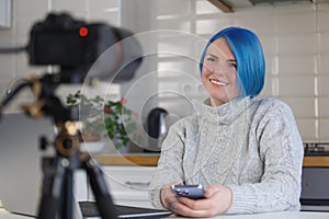 Cheerful blogger talks on video camera. Friendly white woman with blue hair filming an educational course at home