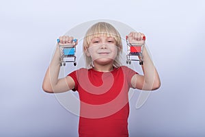 Cheerful blond boy holding in hands two small grocery carts. Baby shopping