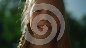 Cheerful blond girl posing in golden sunlight. Playful child looking in camera