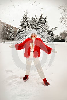 A cheerful blonde in bright red winter clothes throws snow over her head and laughs