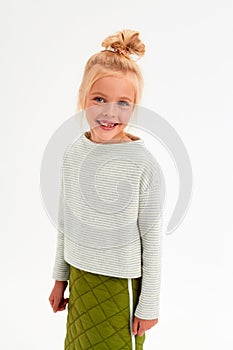 Cheerful blonde girl with a bun on her head smiles with a toothless smile on a white background in a sweater with a strip and a gr