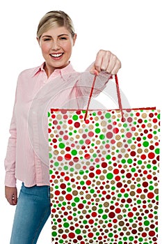 Cheerful blonde girl holding shopping bag in outstretched arm