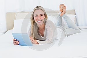 Cheerful blonde using tablet pc on the bed