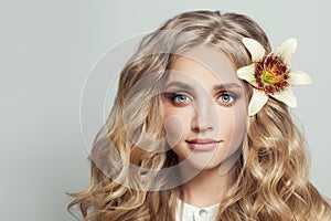 Cheerful blonde woman with healthy clear skin and flower in long curly hair on white