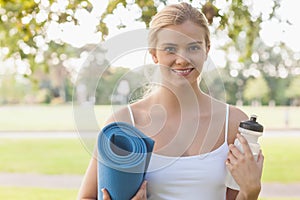 Cheerful blonde woman posing holding an exercise mat