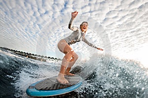 Cheerful blonde woman rides wave on surfboard against cloudy sky background