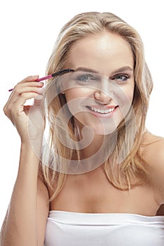 Cheerful blonde woman smiling while using eyebrows comb