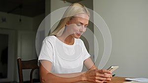 Cheerful blonde young woman using smartphone enjoying watching media in mobile online application, smiling looking to