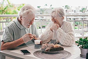 Cheerful bonding senior retired couple enjoy breakfast together sitting outdoors on home terrace. Serene retirement lifestyle