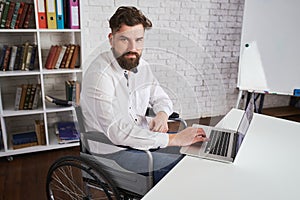 Cheerful boss sitting in a wheelchair and working on a laptop