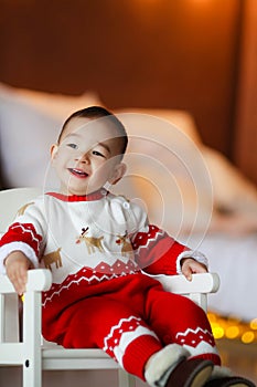 Cheerful boy 2-3 years of Asian appearance in a room at home in a red Christmas suit