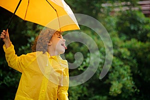 Cheerful boy with a bright yellow umbrella in raincoat.