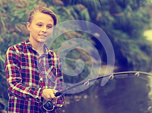 Cheerful boy casting line for fishing on lake