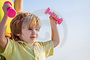 Cheerful boy do exercises with dumbbells. Fitness child. Kid exercising with dumbbells. Sport for little children