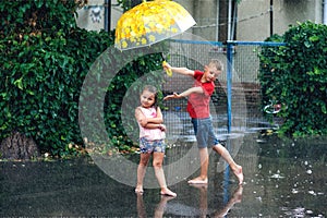 Cheerful boy and girl with umbrella during summer rain