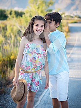 Cheerful boy and girl whispering against nature background.