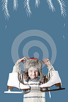 Cheerful boy in a hat with earflaps holding ice skates on blue background