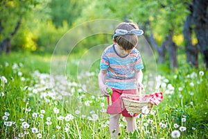 Cheerful boy holding basket full of colorful easter eggs standing on the grass in the park after egg hunt