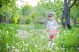 cheerful boy holding basket full of colorful easter eggs standing on the grass in the park after egg hunt