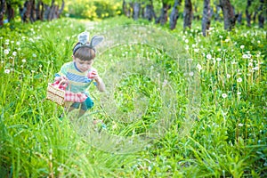 Cheerful boy holding basket full of colorful easter eggs standing on the grass in the park after egg hunt