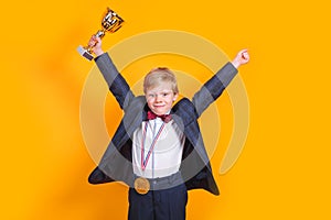 Cheerful boy holding a golden trophy and gold medal on yellow background