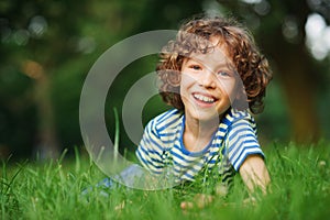 The cheerful boy lies in a dense green grass.