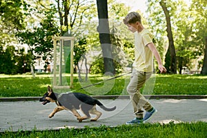 Cheerful boy running with puppy at summer park