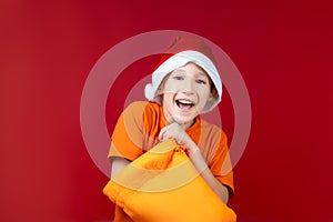 cheerful boy in a Santa hat stuck his hand in a yellow Christmas bag and smiles