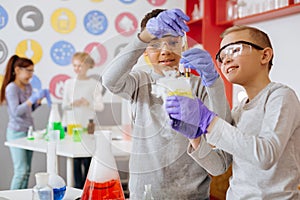 Cheerful boy showing his friend chemical reaction during class