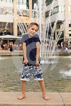 A cheerful boy stands near the fountain. Happy childhood. Parenting, Freedom