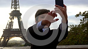 A cheerful boy is taking a photo on the phone on the background of the Eiffel