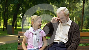 Cheerful boy tells joke to grandfather, laughing together, having fun outdoors