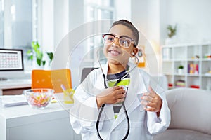 Cheerful boy using stethophone and wearing white jacket of doctor