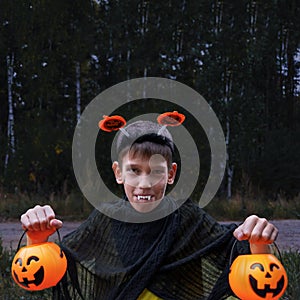 A cheerful boy in vampire costumes shows his teeth holding Jack's lanterns in his hands on a dark background